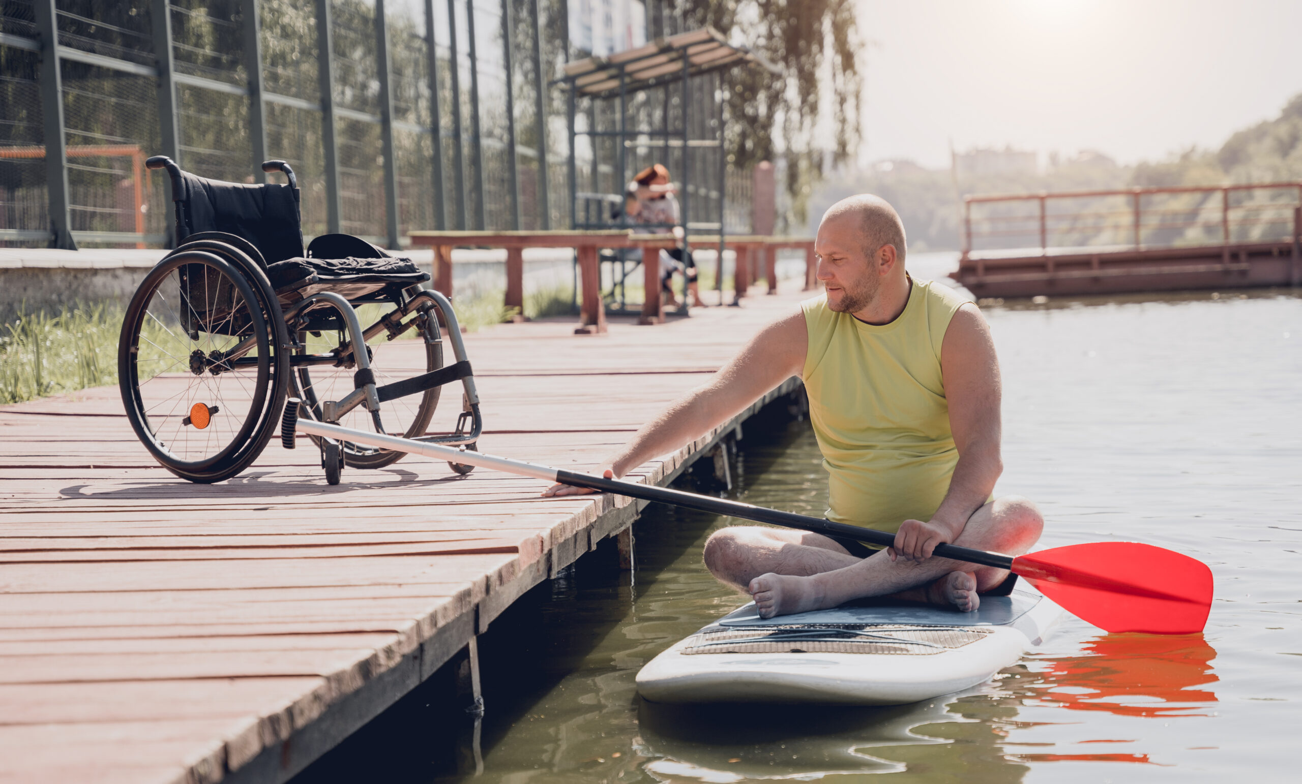 Man on paddleboard next to a wheelchair on a pier.