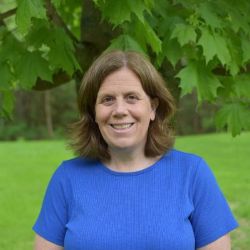 Headshot of Sherie Lizzotte smiling with shoulder length brown hair, wearing a blue shirt