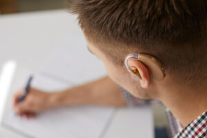 Close up shot of young man with hearing aid writing on paper